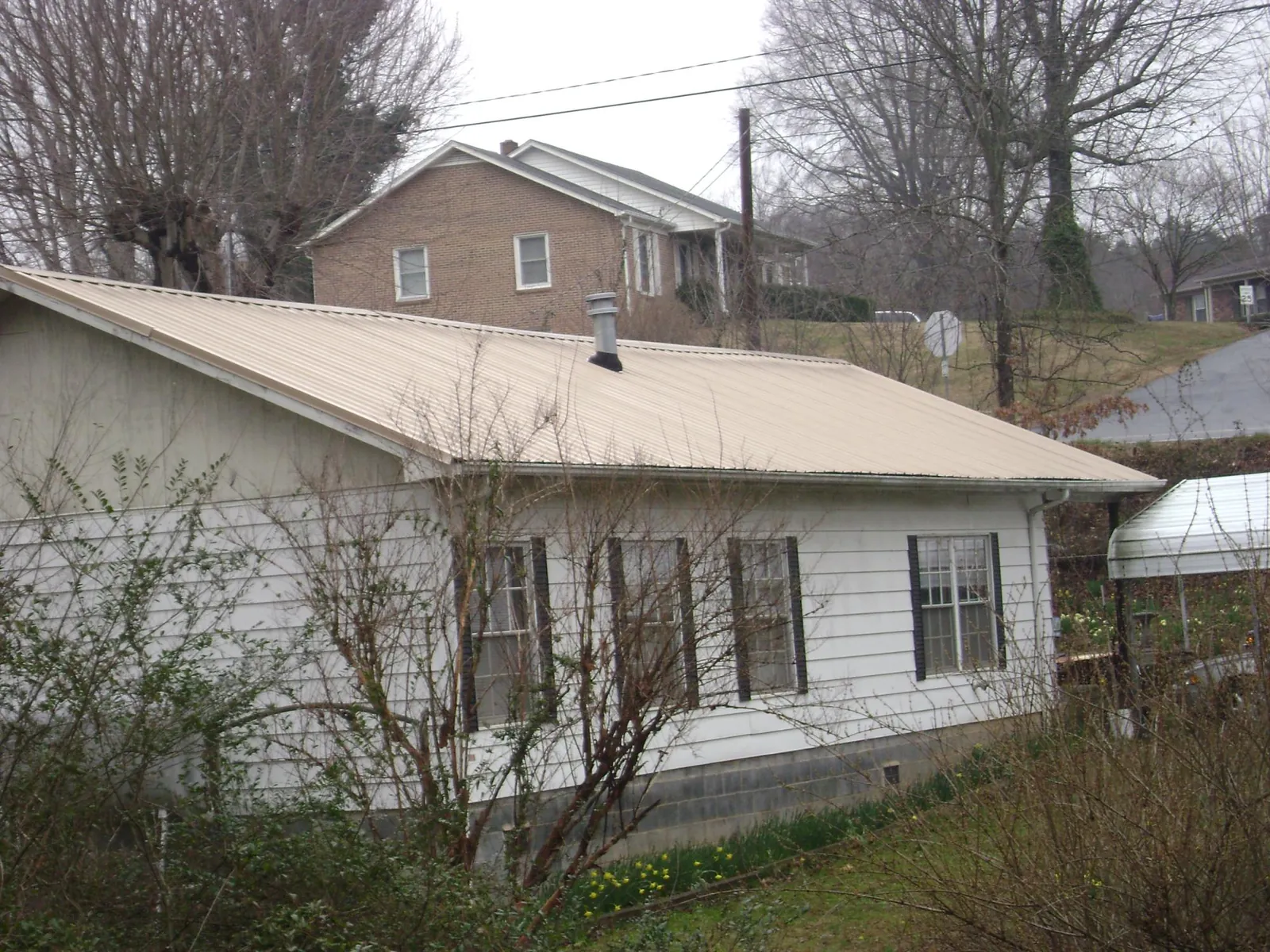 Tan metal roof on a white sided house set into a hillside — Commercial Roofing by Roofing Brothers in Cascade